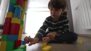 Renkli blokları olan küçük bir çocuk kule inşa ediyor. Çocuk yatak odasında yerde oynuyor. Yaşam tarzı çocukluk yaratıcı gelişimi