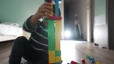 Küçük çocuk yapı taşlarıyla oynuyor. Çocuk yanlışlıkla bloğu düşürdü. Çocuk yatak odasında kule yapıyor.