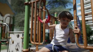 Oyun parkındaki maymun barına tutunan küçük bir çocuk. Aktif çocuk güneşli bir günde dışarıda egzersiz yapıyor.