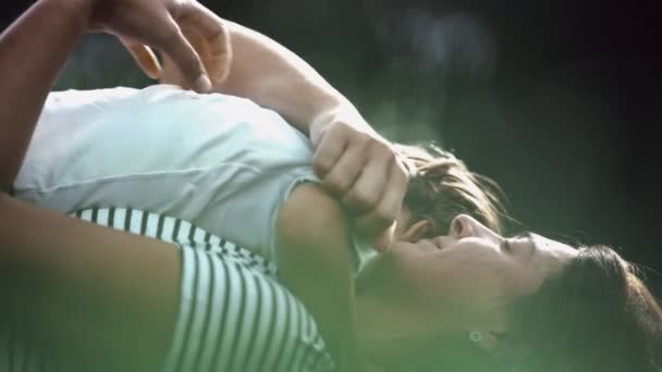 公園で一緒に草の上に寝そべっている子供を抱く母親 母親の愛とケア 太陽の下で親と子供の抱擁 — ストック動画