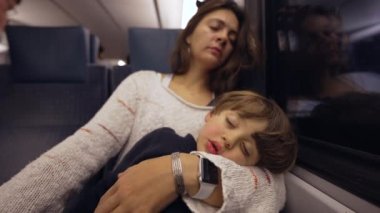 Anne ve çocuk trende uyuyor. Ebeveyn, küçük çocuğu kucaklarken esniyor seyahat ederken birlikte kestiriyor.
