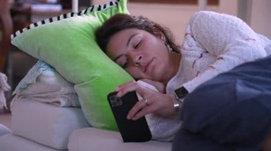 Üzgün bir şekilde kanepede uzanmış telefon ekranına bakan depresif bir kadın. Kanepede oturup içeriği izleyen samimi insan.