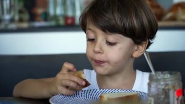 Çocuk kahvaltı masasında yemek yiyor. Küçük çocuğun yakın plan portresi.