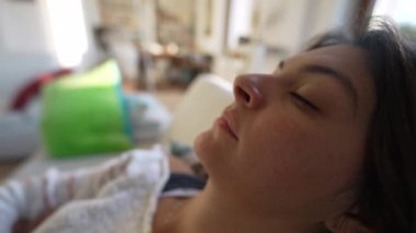 Gözleri kapalı bir kadın. Oturma odasındaki kanepede dinleniyor. Öğlen uykusunda uyuyan kişi