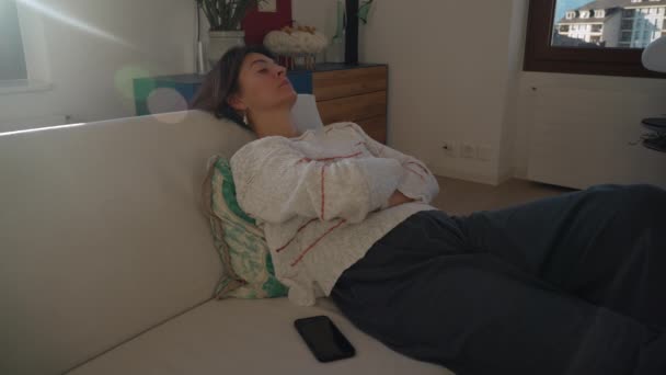 家でゆったりとソファに横になる女性 ソファの上の人午後の日差しのフレアで昼寝をする目を閉じる — ストック動画