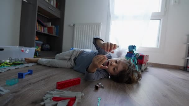 1人でおもちゃで遊ぶ寝室の床に寝そべっている小さな男の子 家で寝そべってる少年が — ストック動画
