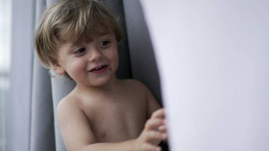 Baby toddler boy hiding behind curtains