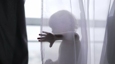 Cute baby toddler standing behind curtain cloth looking at camera