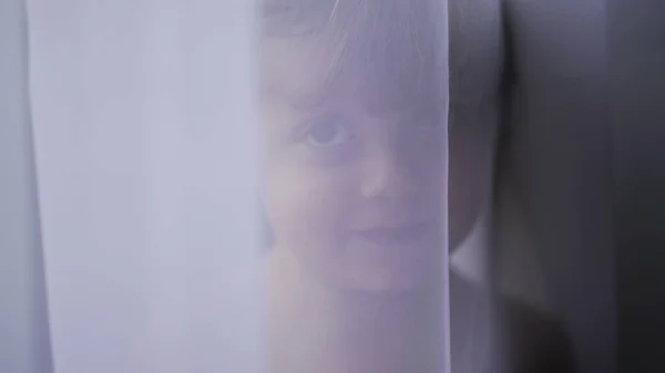 Cute baby toddler standing behind curtain cloth looking at camera