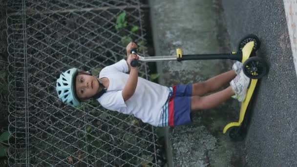 かわいい男の子ポージングのためにカメラともに3輪スクーターとヘルメットスタンドでストリート — ストック動画