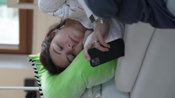 携帯電話の画面をソファの上に寝そべっている退屈な女性 落ち込んでいる人は垂直ビデオでオンラインでソーシャルメディアを閲覧 — ストック動画