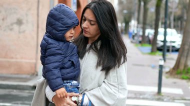 Anne, bebek bebekle dışarıda yürüyor. Siyah maske takıyor.