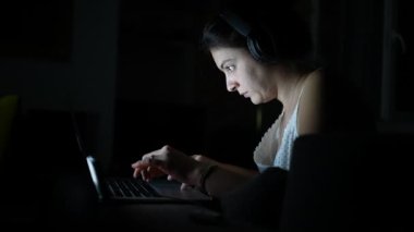 Geceleri dizüstü bilgisayarın önünde çalışan bir kadın. Karanlıkta bilgisayar kullanan ve internette gezinen kişi. Parlak ekranlı samimi modern yaşam tarzı