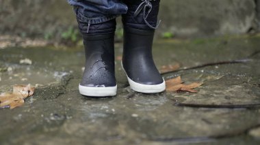 Toddler boy splashes into puddle of water. Child plays with puddles