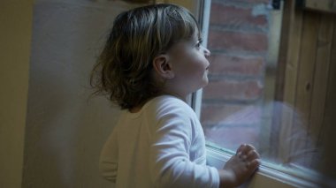Child boy standing by window pointing at something outside