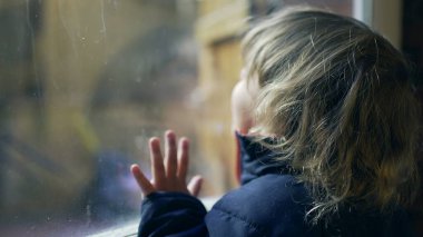 Baby toddler standing by window looking out. Child wanting to go outside