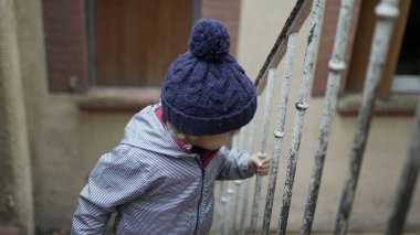 Little baby toddler going up the stairs holding on handrail wearing winter clothes. Child up the stair