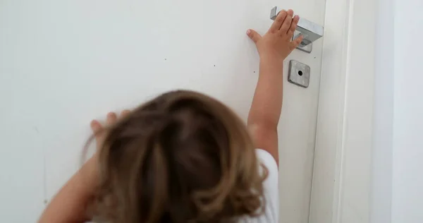 Baby trying to reach door knob. Child on tip toes reaching for door