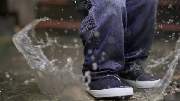 Toddler boy splashes into puddle of water. Child plays with puddles
