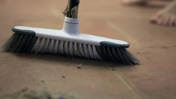 Person sweeps dirty dusty floor with broomstick