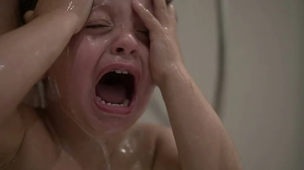 Crying baby washing hair in shower, shampoo itchy eyes in bath. Upset child cries