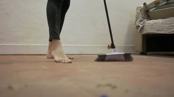 Person sweeping floor with broomstick, dusty dirty floor