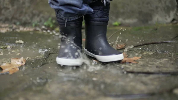 Child jumping into water puddle. Toddler wearing boots splash into puddle