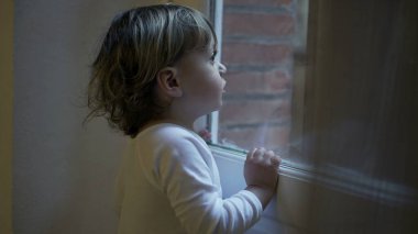 Toddler child staring outside standing by window at home