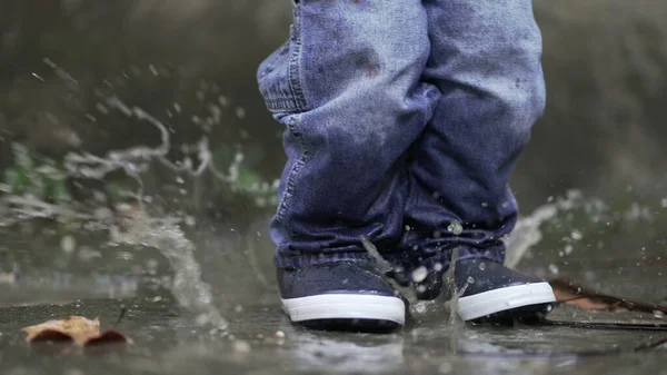 Toddler boy splashes into puddle of water. Child plays with puddles