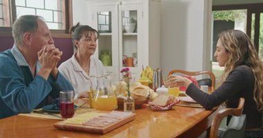 Family at breakfast table. Mature husband and wife talking with young adult daughter in morning meal. Lifestyle casual conversation