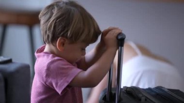 Small boy with travel bag travel suitcase plays with handle doing effort close
