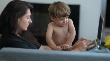 Child wanting mother attention hurting arm. Parent multi tasking working from home in front of laptop. Stressed toddler boy