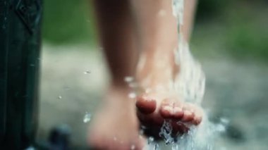 Kid washing feet at water faucet outside. Child cleaning body foot outdoors at park