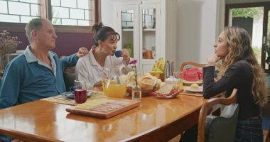 Happy mature parent at breakfast table with adult daughter eating meal in the morning together