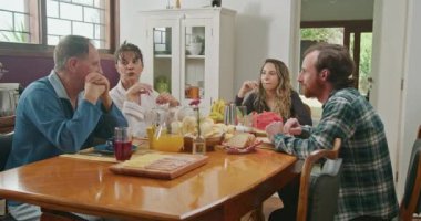 Family eating breakfast together. Mature couple with young adults son and daughter seated at morning table. Older parents and grown adults