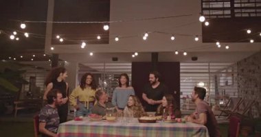 Group of diverse happy friends and family gathered together at home backyard party a night