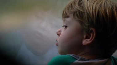 Pensive child traveling by train entering tunnel. Thoughtful small boy passenger staring out window
