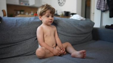 Baby toddler sitting on couch wearing diapers watching Television. One little boy