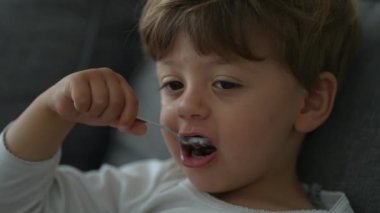 Child eating yogurt with spoon. Close up face of little boy eats nutritious breakfast food