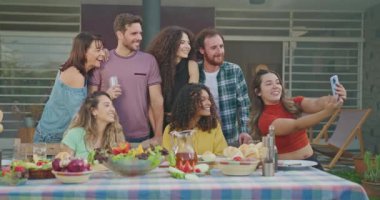 Diverse group of hispanic friends taking selfie together at lunch party in home backyard. Happy group of people take photo with smartphone