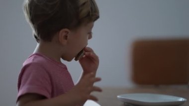 Candid hungry kid wanting food at home breakfast. Messy Child eats piece of bread