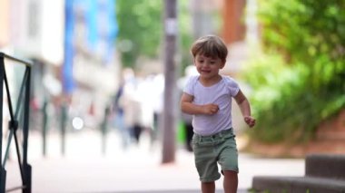 One active little 2 year old boy running outside in city street during summer day. Happy child runner in slow motion