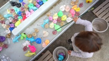 Child fishing plastic ducks at amusement park. Top view of child holding fishing rod having fun at funfair festival party