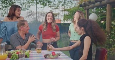 Group of diverse group of people at barbecue party together. Friends enjoying life and food together during sunny day outdoors drinking and eating.