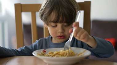 Çatalla makarna yiyen küçük bir çocuk. Çocuk öğle yemeği karbonhidratı yiyor. Çocuk beslenme konsepti
