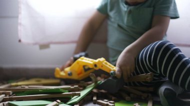 Çocuk buldozer traktör oyuncağıyla oynuyor. Oyun odasında odun topluyor. Kapalı çocuk elleri