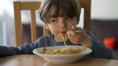 Çatalla makarna yiyen küçük bir çocuk. Çocuk öğle yemeği karbonhidratı yiyor. Çocuk beslenme konsepti