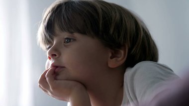 Yüzü birbirine yakın, çenesi içe dönük, düşüncelere dalmış, kamerasız medyayı seyrediyor. Küçük bir çocuğun düşünceli portresi.