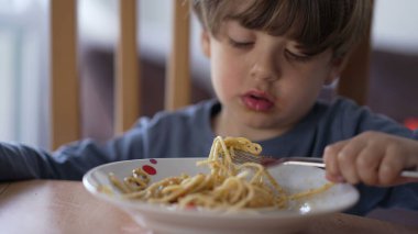 Çatalla makarna yiyen küçük bir çocuk. Çocuk öğle yemeği karbonhidratı yiyor. Çocuk beslenme konsepti
