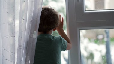 Karlı bir günde pencerenin yanında duran bir çocuk. Küçük çocuk kış mevsiminde camın kenarında durur ve dışarıya bakar.